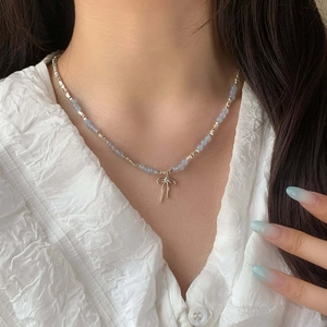 Close-up of a light blue beaded necklace with a silver bow pendant on a female model