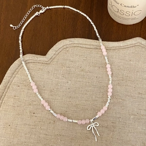 Elegant beaded necklace with pink stones and silver bow pendant on a rustic background