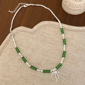 Detail of green beaded necklace with silver bow pendant on a rustic wooden background