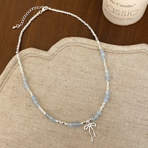Close-up of beaded necklace with light blue stones and hollow bow pendant on wood surface