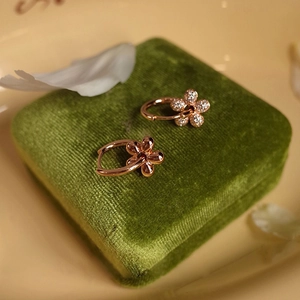 Close-up of rose gold flower earrings with pavé diamonds on a green velvet box
