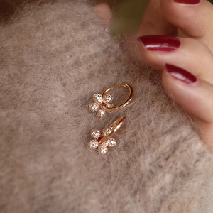 Rose gold flower earrings with white crystals and red center stones on warm sweater