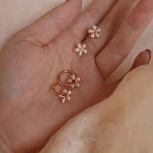 Detail of rose gold flower earrings with white pavé zircons on soft pink fabric