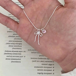 Macro view of silver bow necklace with pink heart crystal on a snake bone chain