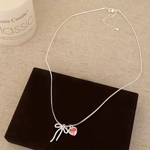 Detail of silver bow and pink heart pendant necklace on velvet box display