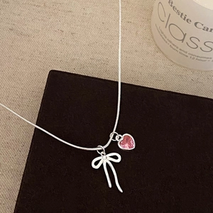 Detailed close-up of a silver bow and pink heart pendant on a delicate snake chain