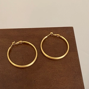Détail de boucles d'oreilles créoles torsadées dorées avec texture mate brossée