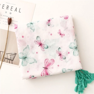 Dettaglio di sciarpa in lino con stampe di farfalle rosa e nappe turchesi