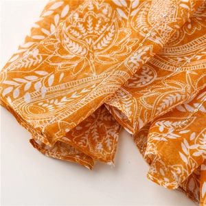 Macro detail of hand-sewn golden sequins and ethnic floral print on orange cotton scarf