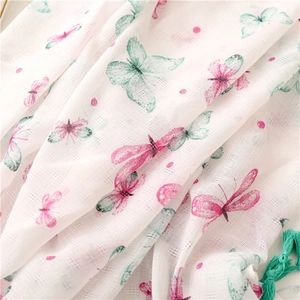Dettaglio di sciarpa in cotone bianco con stampe di farfalle rosa e nappe verdi