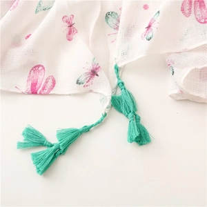 Dettaglio di sciarpa in cotone bianco con stampa farfalle rosa e nappe verdi