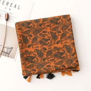 Dettaglio della sciarpa arancione mattone con motivo paisley e nappe decorative