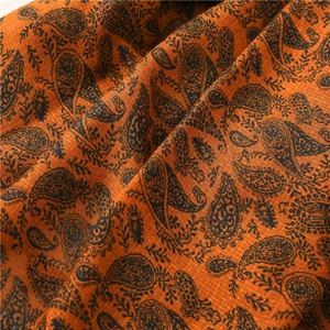Dettaglio di una sciarpa in cotone e lino arancione con motivo paisley nero e frange