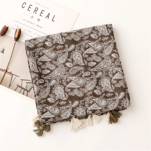 Dettaglio di sciarpa marrone con motivo paisley e morbide nappe su sfondo minimalista