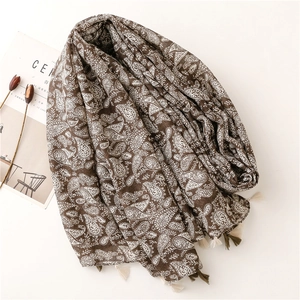 Dettaglio di sciarpa in cotone marrone con motivo paisley e nappe decorative ai bordi