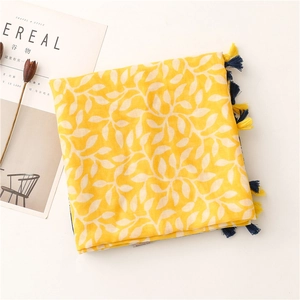 Détail d'une écharpe jaune en coton et lin avec motifs de feuilles et pompons colorés