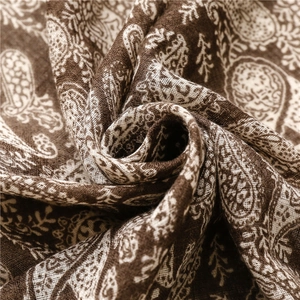 Dettaglio di una morbida sciarpa in cotone marrone con motivi paisley bianchi e floreali