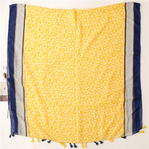 Détail d'une écharpe jaune à motif de feuilles avec bordure géométrique bleue et franges