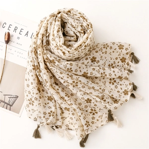 Dettaglio di sciarpa in cotone albicocca con motivo floreale e nappe decorative marroni