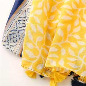 Détail d'une écharpe jaune à feuilles tropicales, pois et pompons à franges assortis