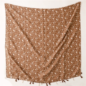 Dettaglio di sciarpa in cotone marrone con fiori bianchi e bordi con frange