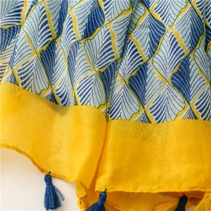 Detail eines gelben Baumwollschals mit blauen Blattmustern und feinen Fransenquasten