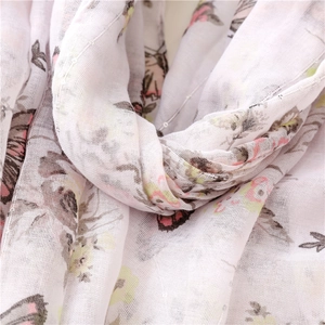 Detailed macro view of soft white scarf with delicate pink butterfly patterns and fringe