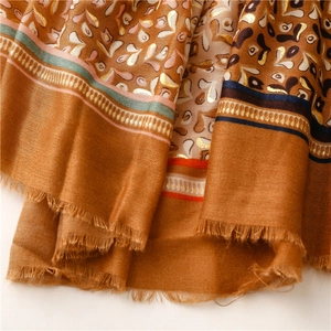 Detailed close-up of soft scarf featuring intricate gold foil patterns and fringe edges