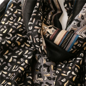 Close-up of black scarf featuring golden paisley patterns and striped border detail