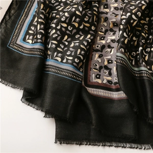 Detail of black cotton-linen scarf with golden paisley print and frayed tassel edges