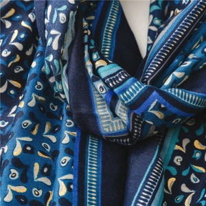 Close-up of bohemian scarf with abstract leaves, geometric stripes, and gold glitter detail