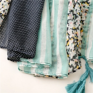 Macro detail of scarf featuring green floral, dots, stripes patterns and tassel fringe