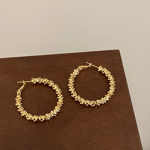 Détail de boucles d'oreilles créoles torsadées dorées avec texture tressée riche