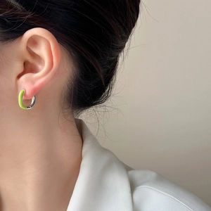 Detail of lime green and silver C-shaped enamel earrings worn by a model in a minimal setting