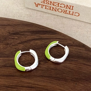 Detail of silver hoop earrings with lime green enamel on a wooden tray surface