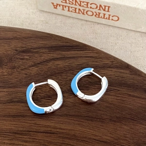 Detail of square sky blue enamel hoop earrings in silver metal on a wood tray