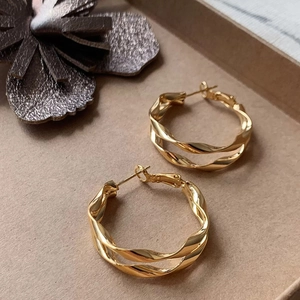 Dettaglio macro di orecchini a cerchio a doppia spirale placcati oro con finitura lucida