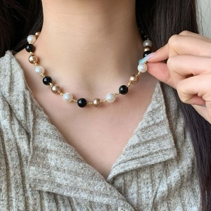 Vintage style necklace with black onyx, white pearls, and gold accents worn by a model