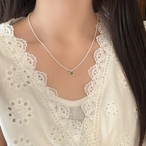 Sparkling silver chain necklace with a round green gemstone pendant on a female model