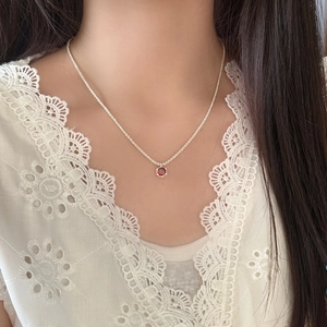 Elegant silver necklace with a round red zircon pendant worn on a white lace blouse