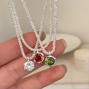 Close-up of three sparkling zircon necklaces in clear, red, and green with silver twist chains