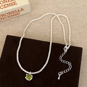 Detail of silver chain necklace featuring green zircon pendant and lobster clasp closure