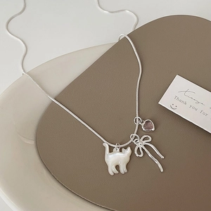 Dettaglio collana argento con ciondoli gatto, fiocco e cuore rosa su piatto ceramica
