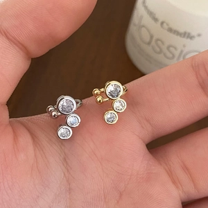 Bagues d'oreilles minimalistes en or et argent avec trois zircons présentées à la main