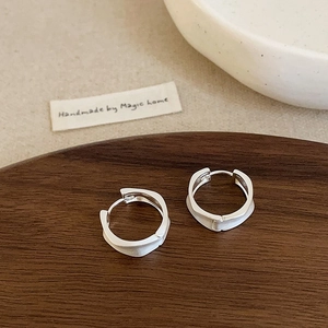 Close-up of matte silver irregular wave hoop earrings on a dark wood tray