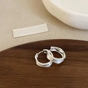 Detail of matte silver wave hoop earrings on a dark wooden display tray