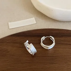 Detail of silver matte brushed hoop earrings with wide textured metal on wooden tray