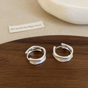 Macro detail of silver irregular wavy textured hoop earrings on a dark wooden tray