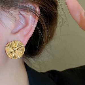Close-up of gold wavy textured round stud earrings with a spherical center on ears