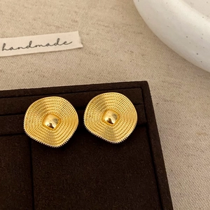 Detail of wavy gold earrings with concentric circular textures on a jewelry stand